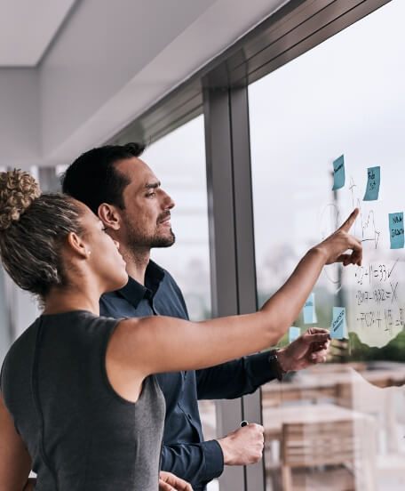 two colleagues reviewing notes on sticky pads stuck to a window